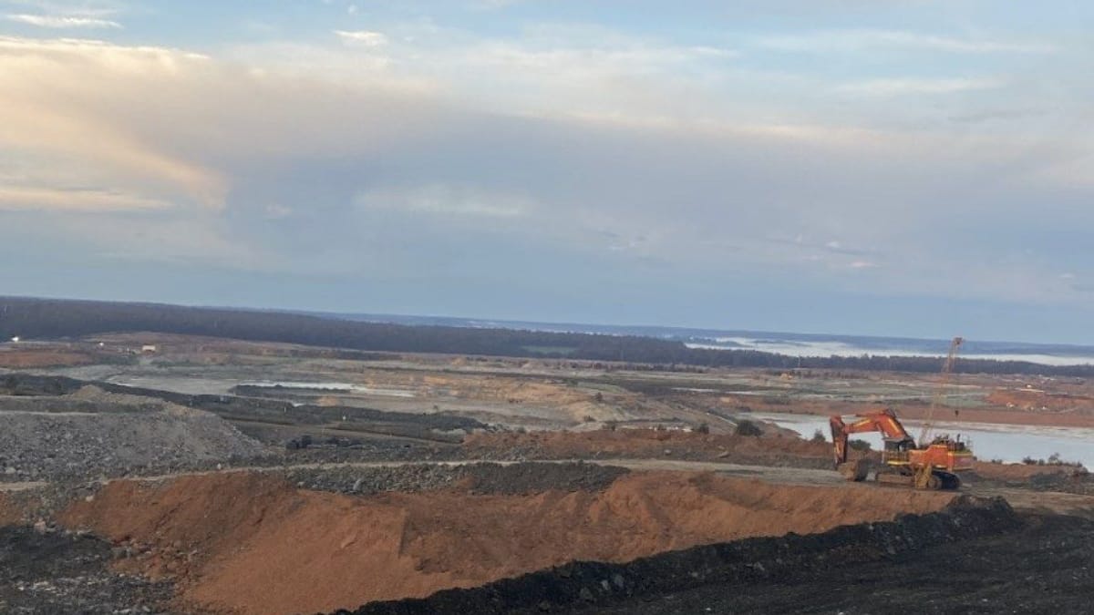 Large-scale mine earthworks and tailings landscape at dusk with an excavator working the pit edge